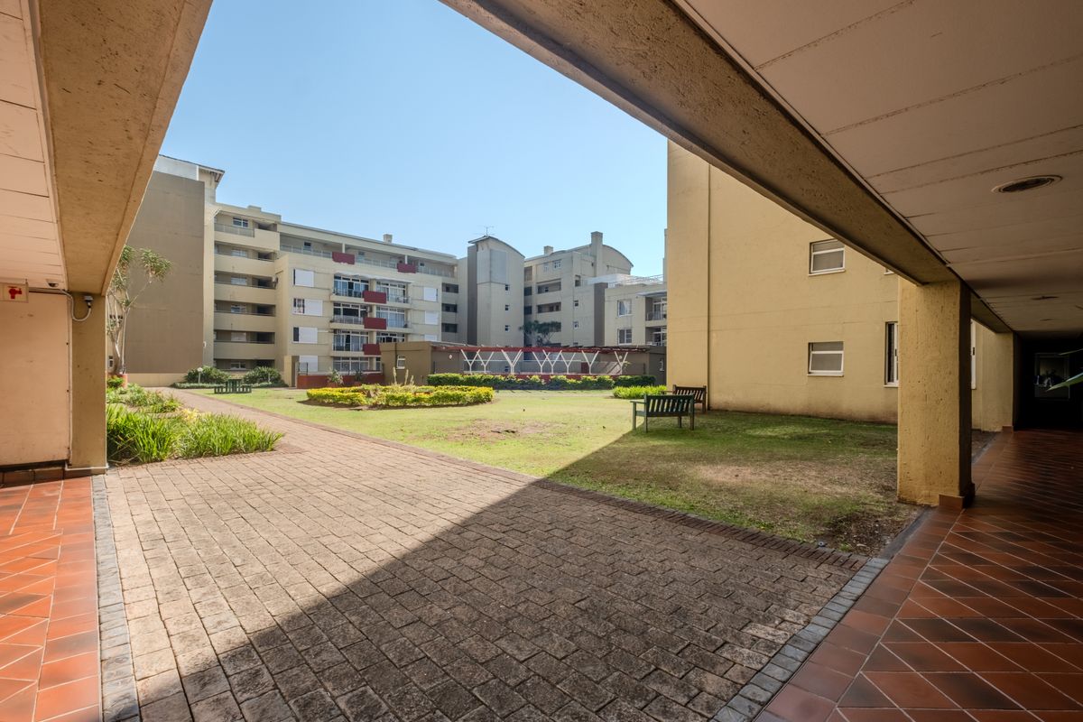 A view of the communal garden and paved courtyard area from the covered walkway of the apartment complex.
