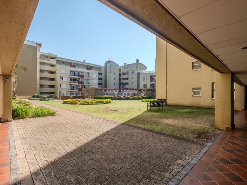 A view of the communal garden and paved courtyard area from the covered walkway of the apartment complex.
