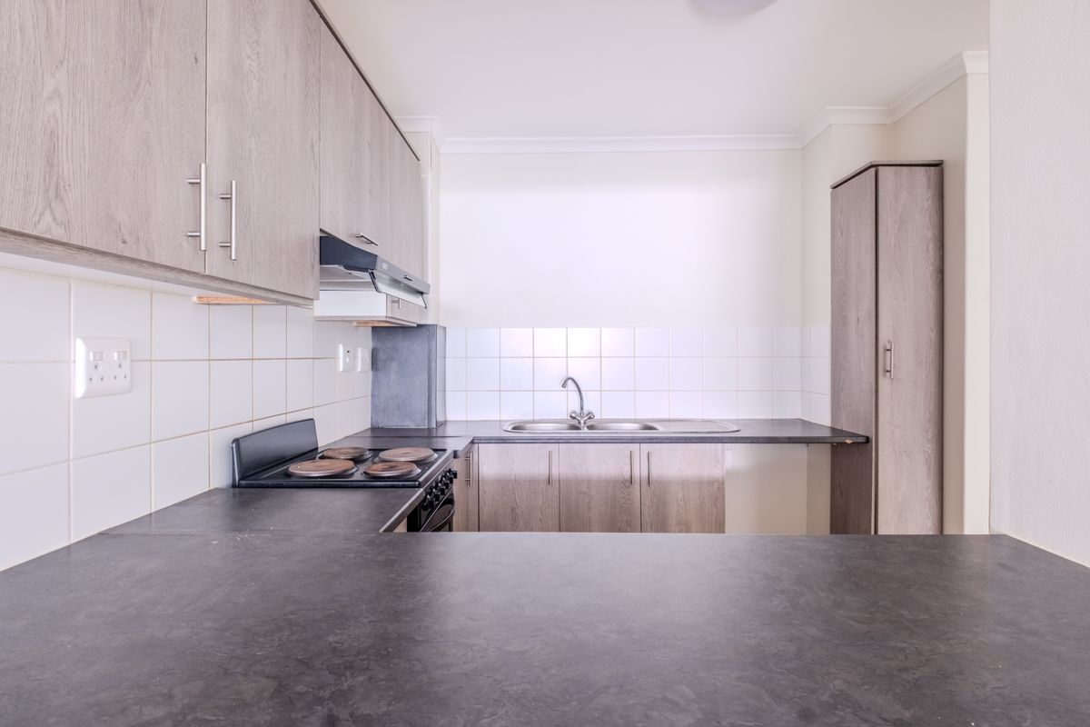 A clean, functional kitchen featuring light wood-tone cabinetry, dark laminate countertops, a built-in electric stove, and a stainless steel sink with tiled backsplash.