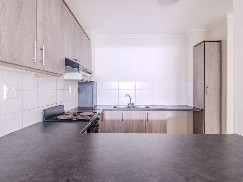 A clean, functional kitchen featuring light wood-tone cabinetry, dark laminate countertops, a built-in electric stove, and a stainless steel sink with tiled backsplash.