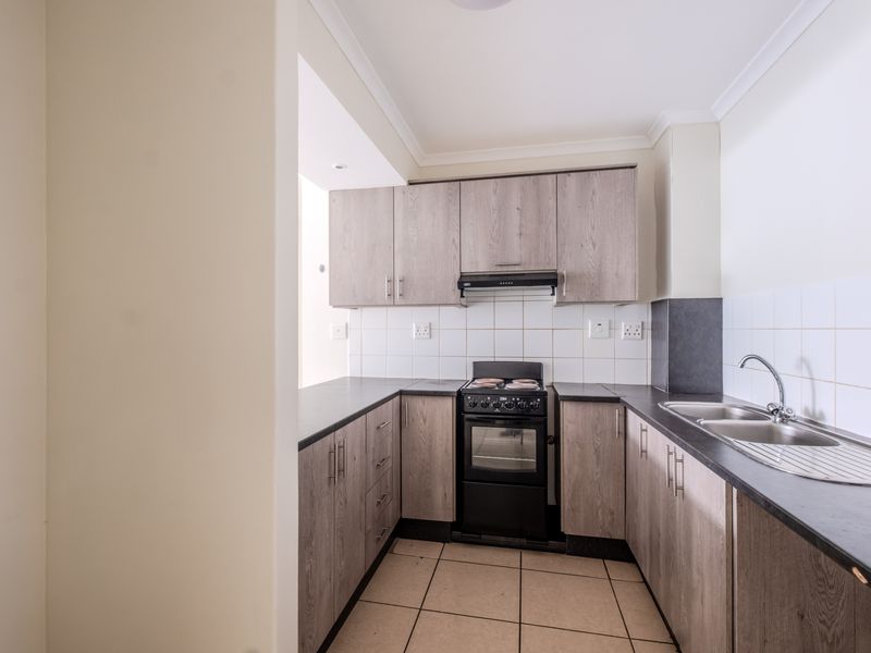 A functional kitchen featuring wood-look laminate cabinetry, dark countertops, a freestanding stove with extractor fan, and tiled flooring.