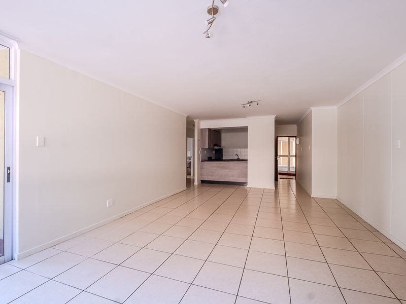 Spacious open-plan living area featuring neutral tiled flooring, ample natural light, and a functional kitchen nook with built-in cabinetry.