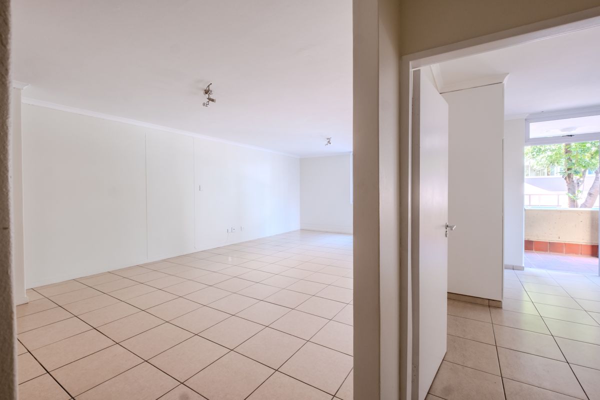 A bright, empty living area featuring neutral tiled flooring and direct access to an outdoor balcony space.