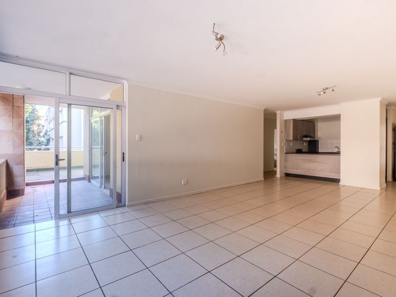 Spacious open-plan living area featuring tiled floors, neutral walls, and direct access to a private balcony, adjacent to a functional kitchen space.