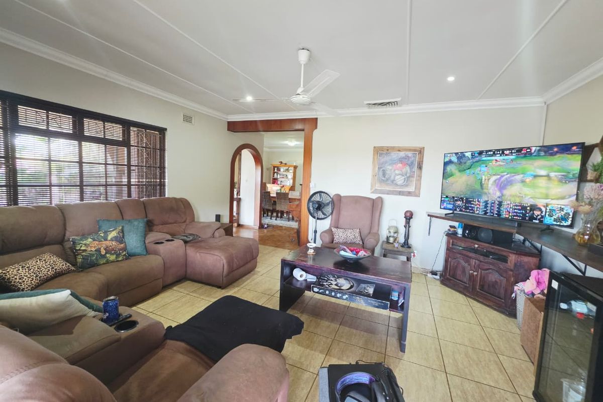 Spacious living room featuring tiled flooring, a ceiling fan, and an open archway leading to the dining area.
