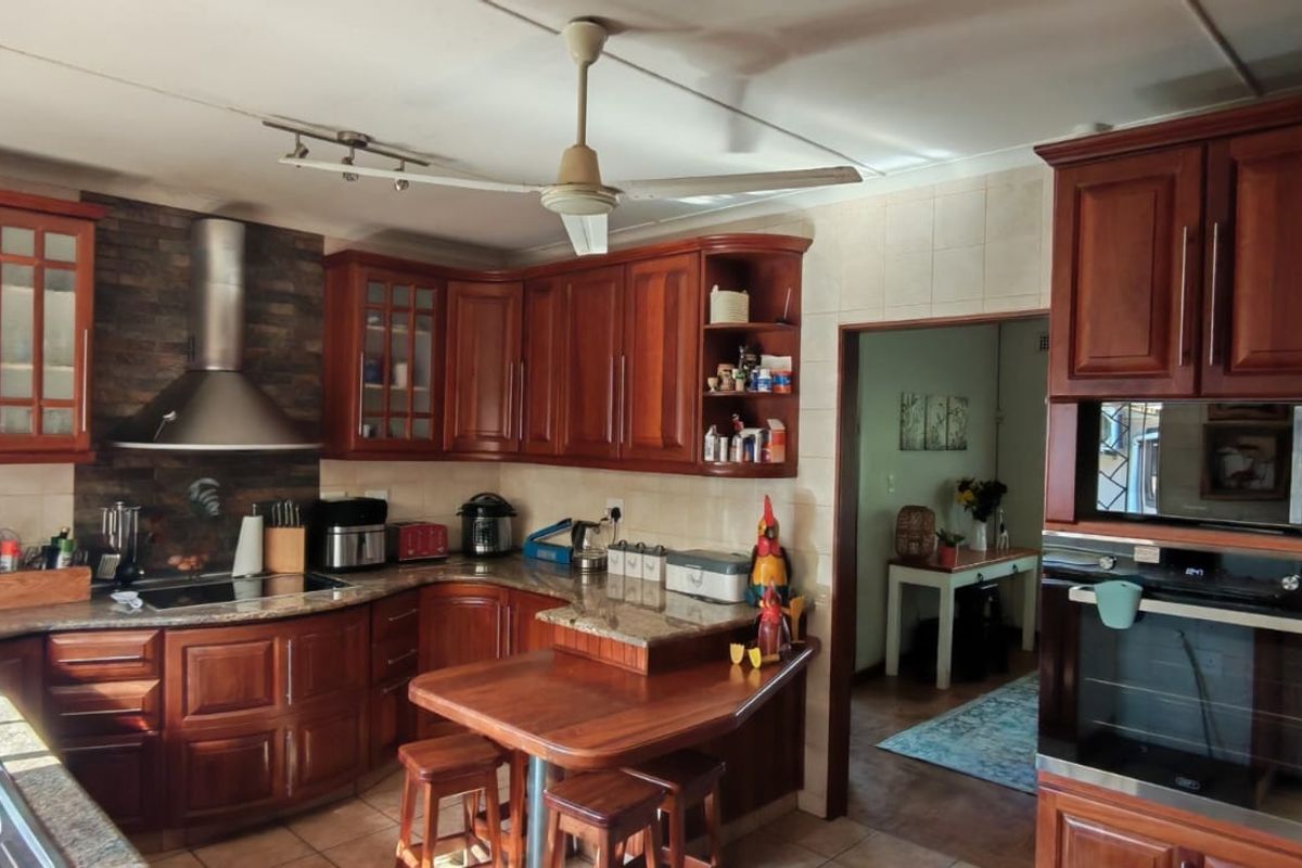 A functional kitchen featuring warm-toned wooden cabinetry, granite countertops, built-in oven and microwave, and a stainless steel extractor fan.