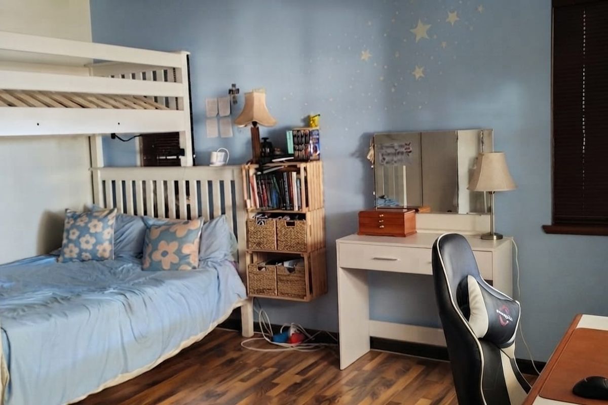 A functional bedroom featuring laminate flooring and window blinds, currently set up with a bunk bed and study area.