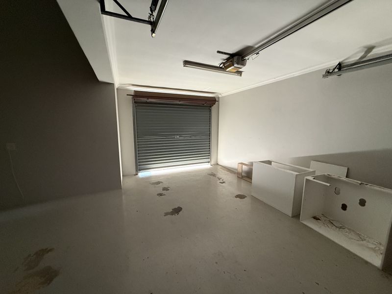 A spacious, empty garage featuring a roller shutter door, garage door motor, and concrete flooring, offering ample storage or parking space.