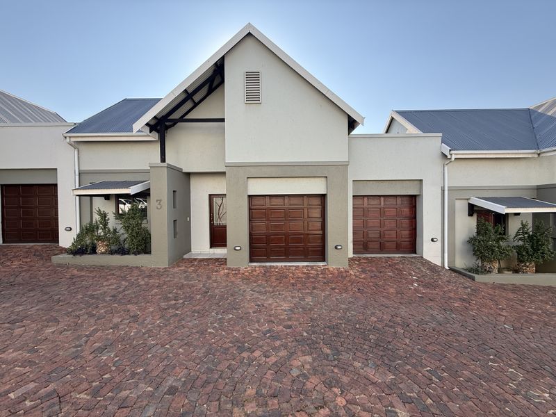 Front elevation of a modern townhouse featuring a double garage with timber doors, a cobblestone driveway, and a distinctive gabled roofline.