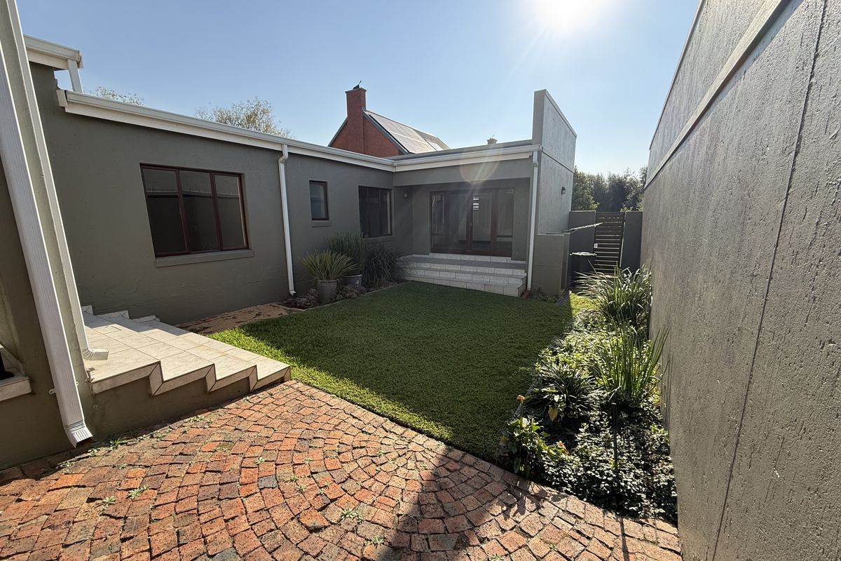 A well-maintained rear courtyard featuring a brick-paved patio, tiled steps, and a neat lawn area enclosed by boundary walls.