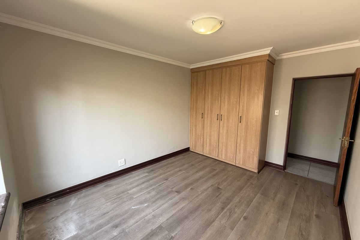 A clean, empty bedroom featuring wood-look laminate flooring, neutral walls, and built-in wooden cupboards, offering a versatile space ready for personalization.