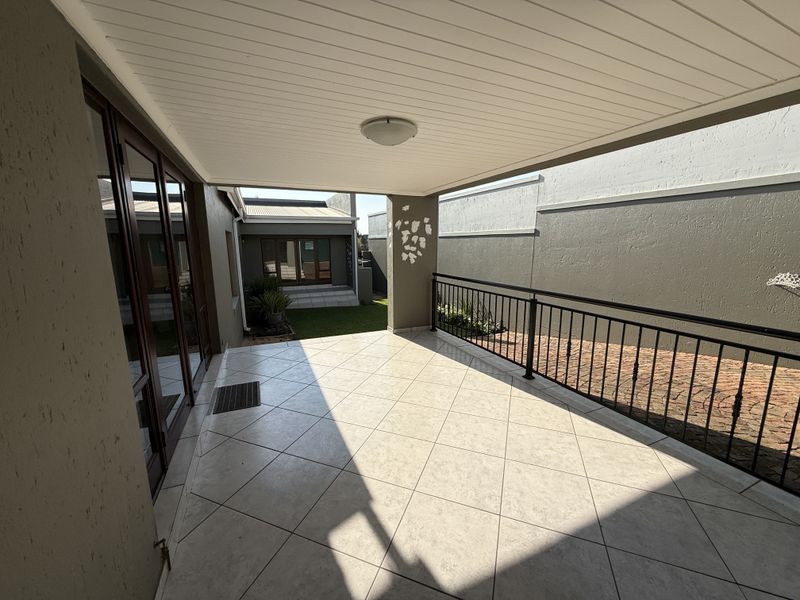 A spacious covered patio featuring tiled flooring, a metal balustrade, and direct access to the garden through sliding glass doors.