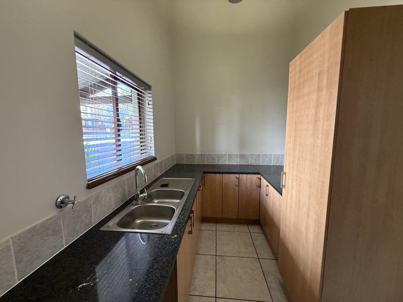 A functional scullery featuring granite countertops, double bowl stainless steel sink, built-in cabinetry, and tiled flooring, providing ample prep and storage space.