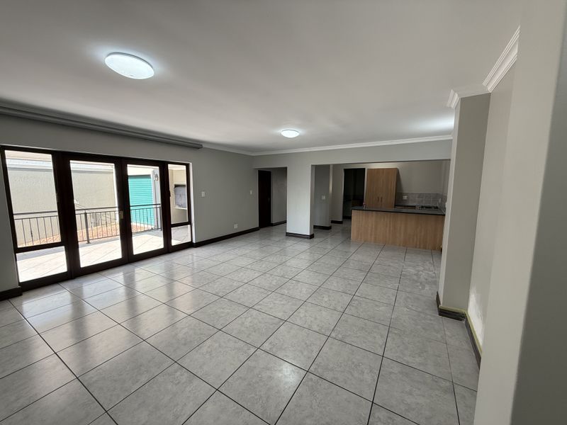 Spacious open-plan living and kitchen area featuring neutral ceramic tiling, built-in cabinetry, and large sliding doors leading to an outdoor balcony.