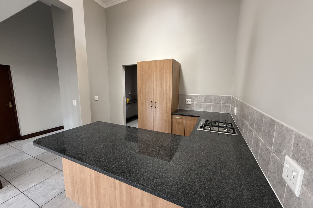 A clean, modern kitchen featuring granite countertops, a built-in gas hob, and ample cabinetry, with neutral tiled flooring and a tiled backsplash.