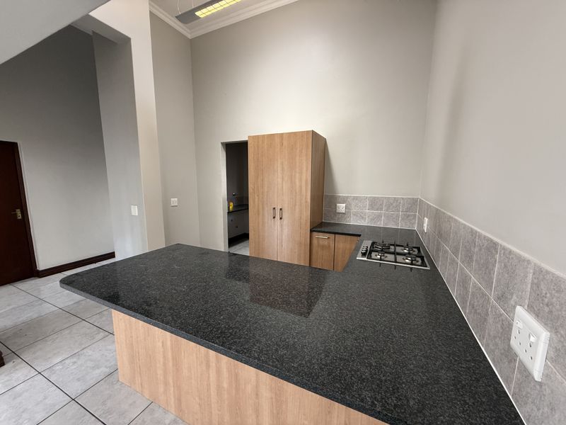 A clean, modern kitchen featuring granite countertops, a built-in gas hob, and ample cabinetry, with neutral tiled flooring and a tiled backsplash.