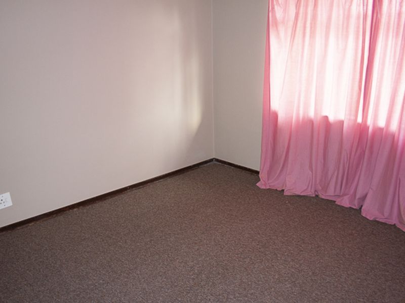 An empty bedroom featuring neutral wall paint, carpet flooring, and a window with pink curtains.