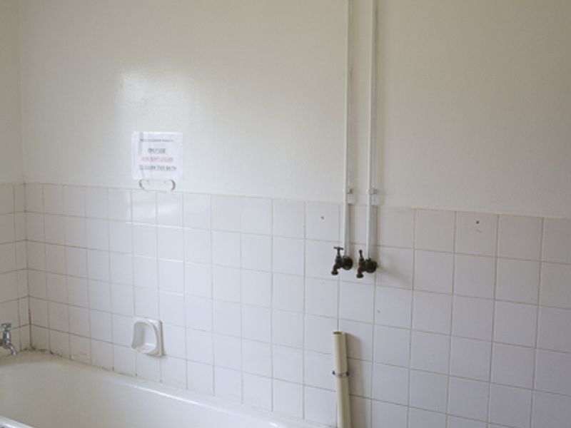 A dated bathroom featuring a tiled bathtub, exposed plumbing fixtures, and white wall tiles. The space is vacant and requires cosmetic updates.