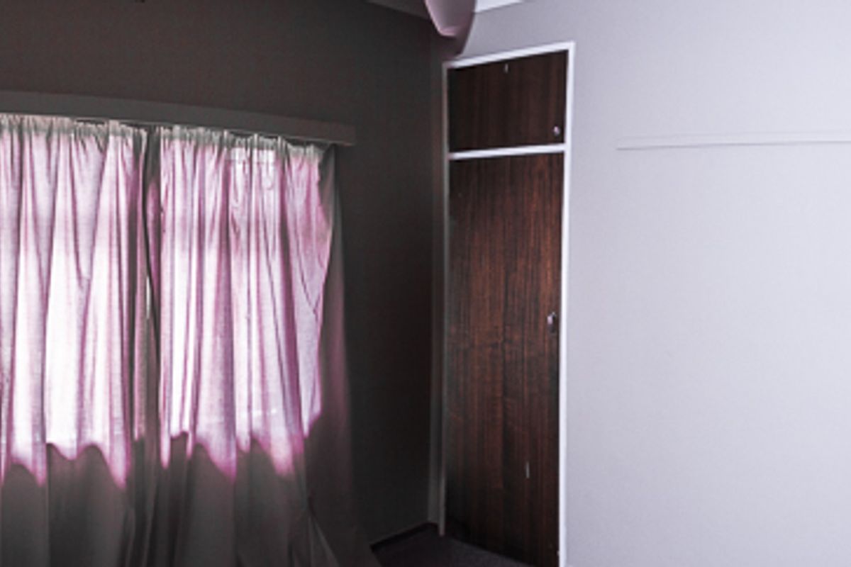 A vacant bedroom featuring a built-in wooden cupboard and a window with a curtain rail.