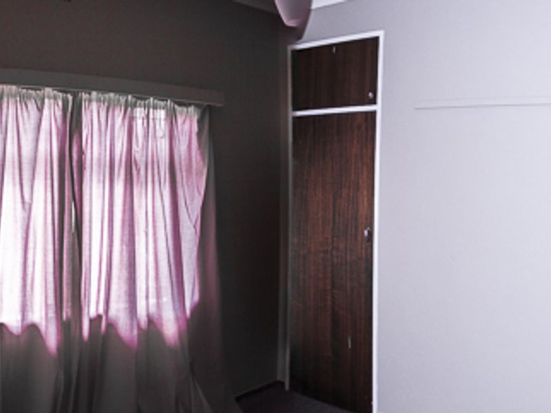 A vacant bedroom featuring a built-in wooden cupboard and a window with a curtain rail.