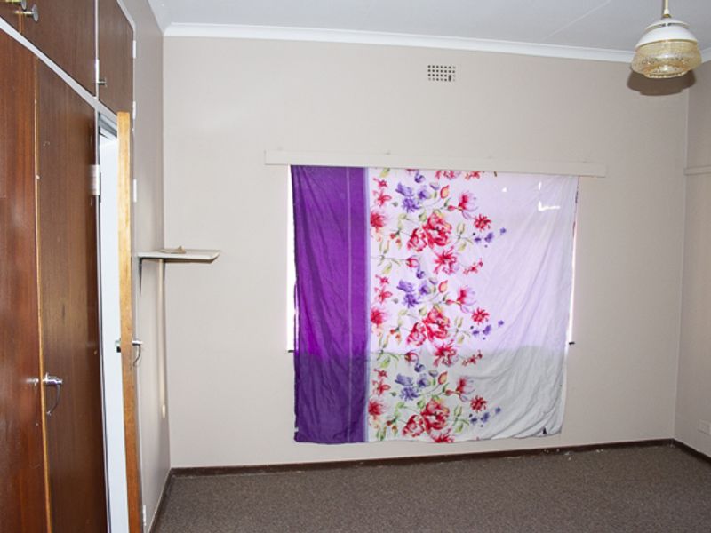 A vacant bedroom featuring built-in wooden cupboards, carpeted flooring, and a central ceiling light fixture, offering a blank canvas for renovation.
