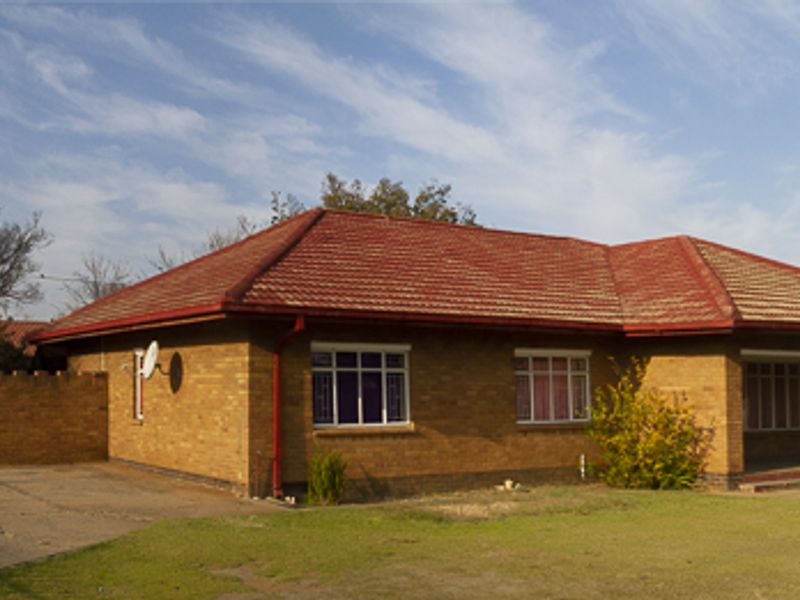 Front view of a single-story brick house featuring a tiled roof, attached garage, and a concrete driveway set on a residential plot.