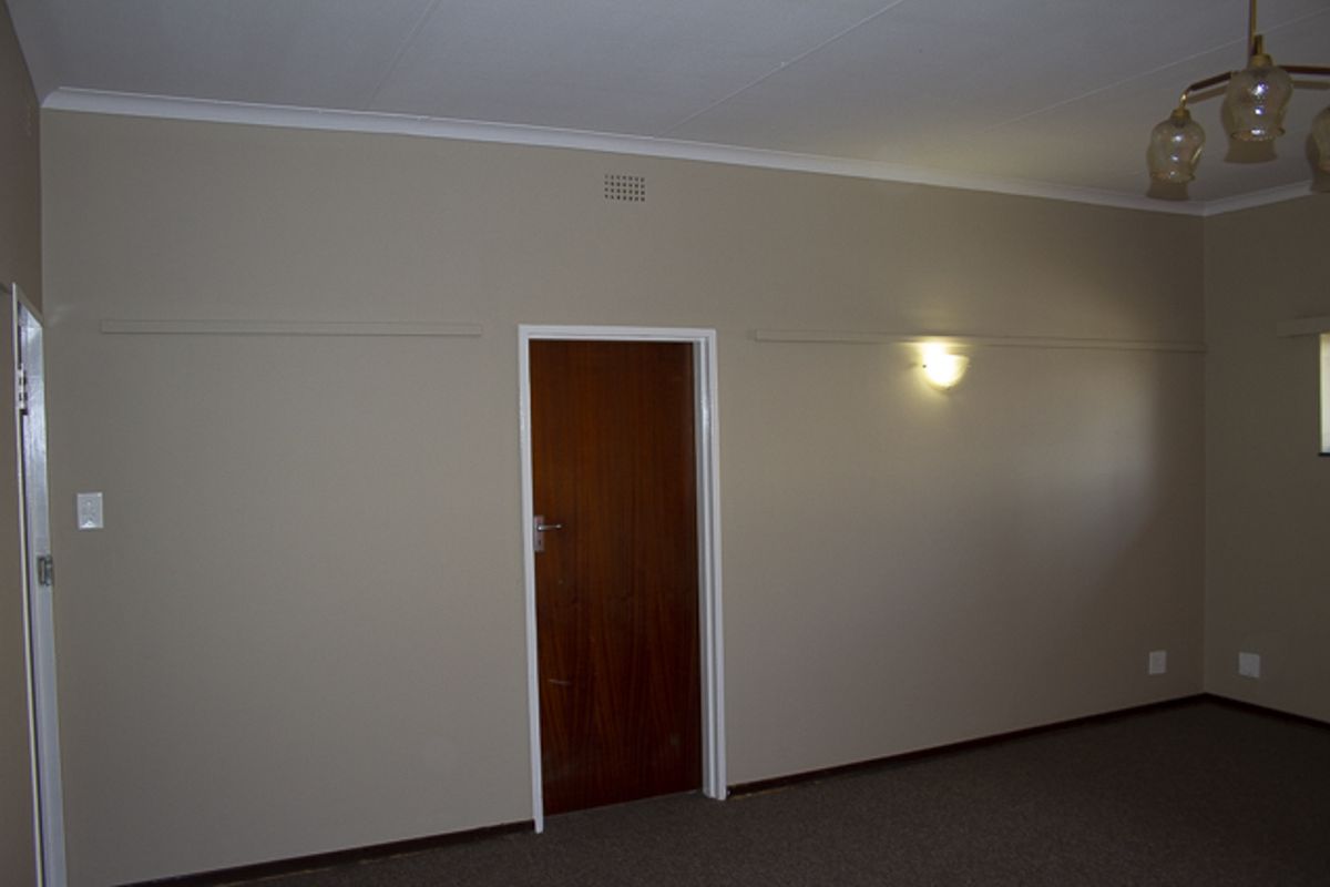 An empty living room featuring neutral walls, carpet flooring, and a timber door, providing a blank canvas for interior design updates.