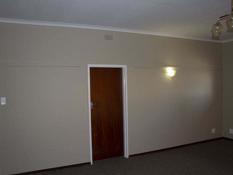 An empty living room featuring neutral walls, carpet flooring, and a timber door, providing a blank canvas for interior design updates.