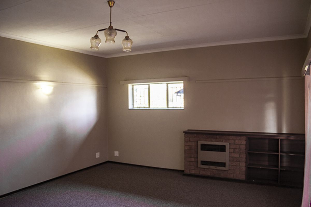 A spacious, empty living room featuring a brick fireplace with integrated shelving, neutral wall tones, and carpeted flooring.