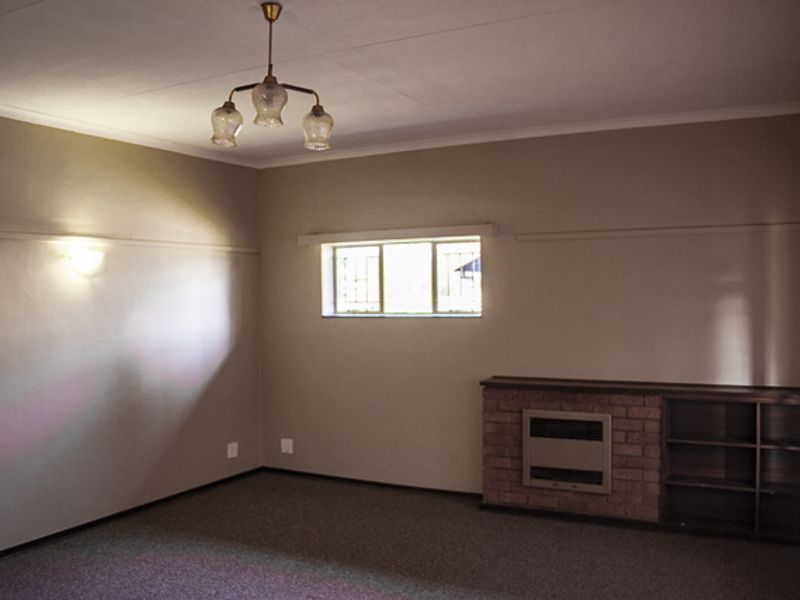 A spacious, empty living room featuring a brick fireplace with integrated shelving, neutral wall tones, and carpeted flooring.