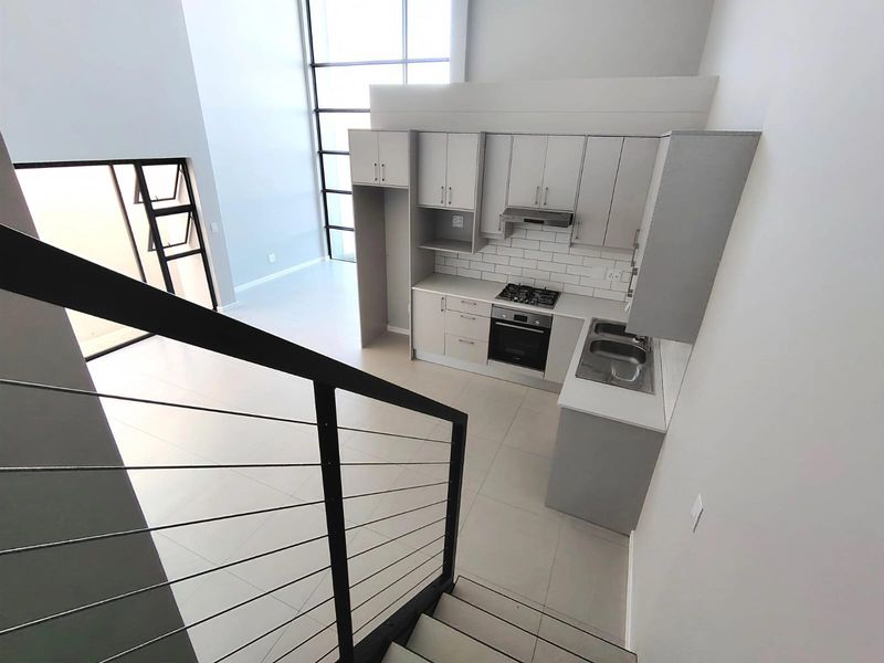 Modern open-plan kitchen featuring sleek cabinetry, built-in appliances, and subway tile backsplash, overlooking a bright living area with high ceilings and large windows.
