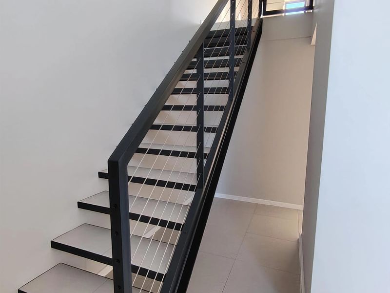 Modern staircase featuring a sleek black metal frame with cable railing and neutral tiled flooring in a clean, minimalist hallway.