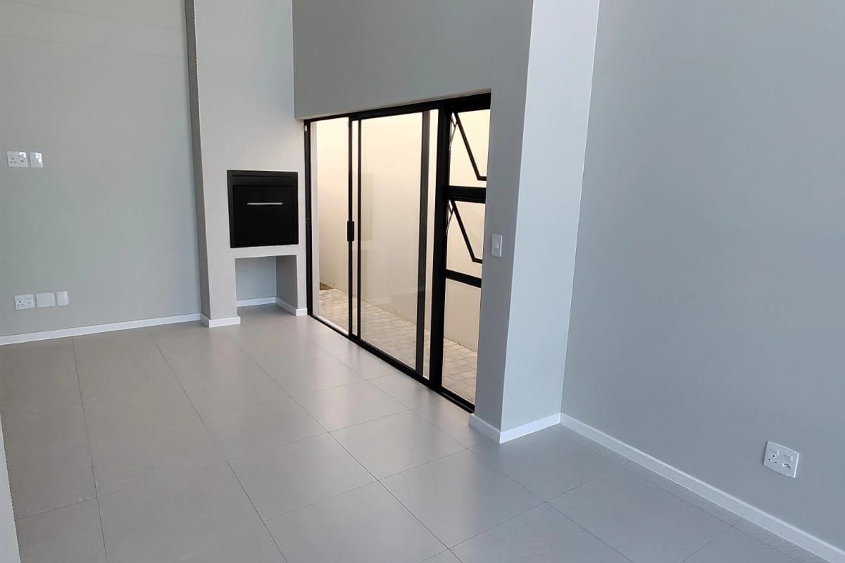 A bright, modern, and empty living area featuring high ceilings, tiled flooring, and a built-in fireplace with access to an outdoor space.