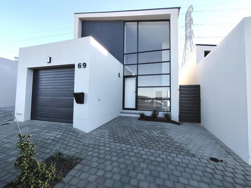 Modern two-story residential facade featuring a sleek garage, paved driveway, and a striking full-height glass entrance.