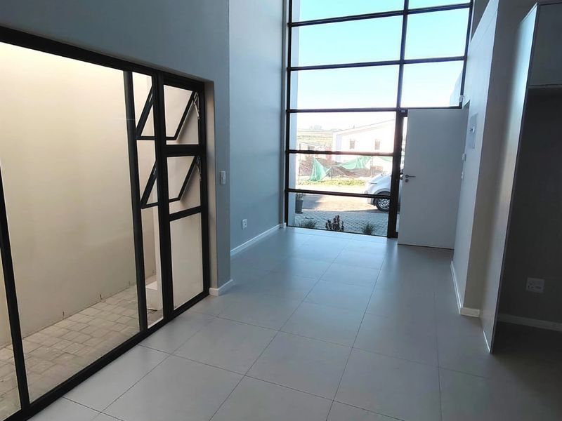 A bright, modern entrance hall featuring double-volume ceilings, large floor-to-ceiling windows, and sleek tiled flooring with an adjacent internal courtyard view.