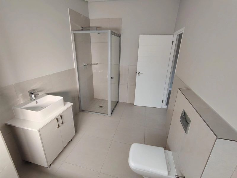 Modern bathroom featuring a glass shower enclosure, wall-mounted toilet with concealed cistern, and a contemporary vanity unit with a vessel sink.