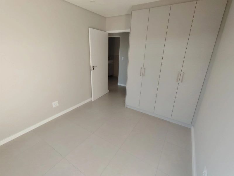 A clean, neutral bedroom featuring large-format floor tiles, built-in cupboards, and a doorway leading to an adjacent space.