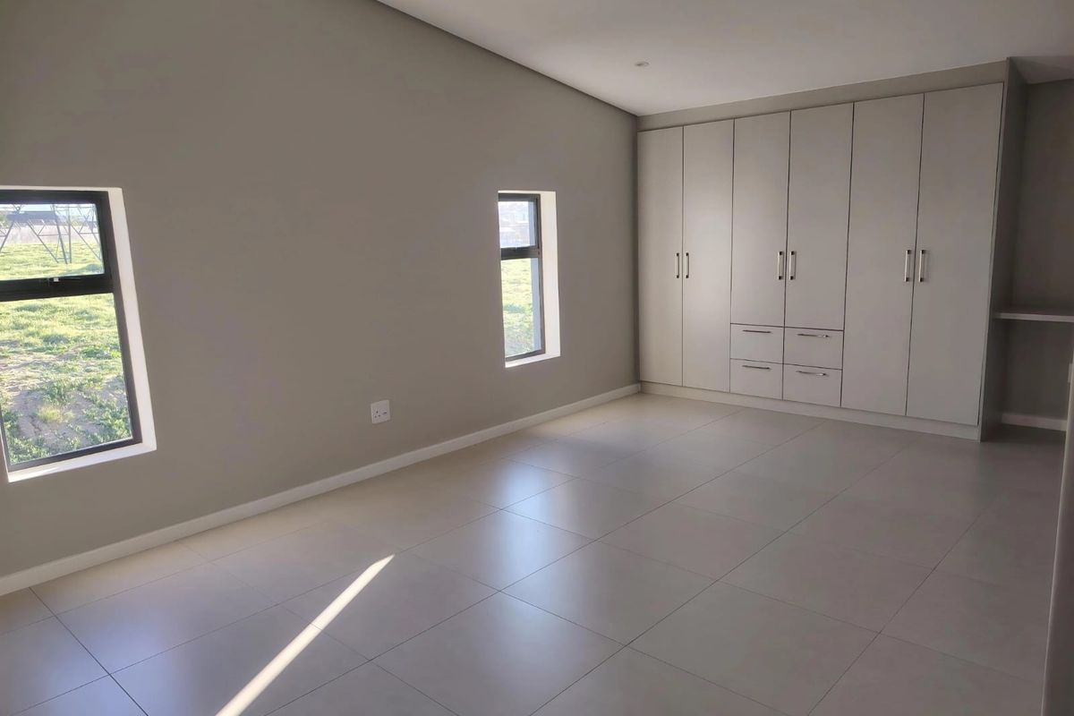 A spacious, modern bedroom featuring neutral tiled flooring, built-in cupboards, and large windows providing ample natural light.