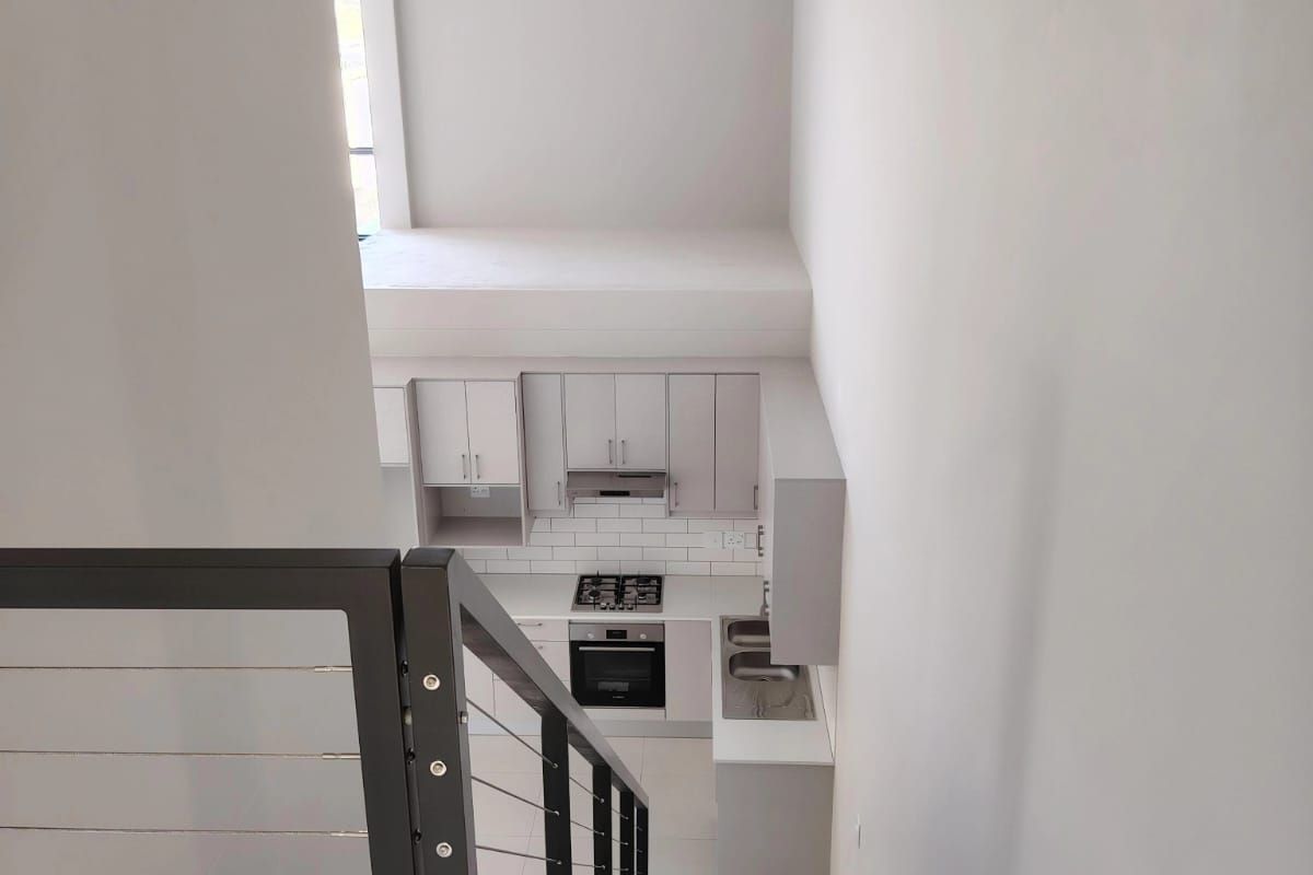 A modern, minimalist kitchen viewed from the staircase, featuring sleek cabinetry, integrated appliances, and a clean subway tile backsplash in an open-plan layout.