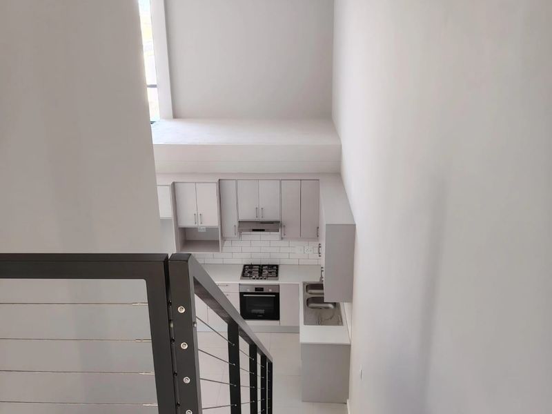A modern, minimalist kitchen viewed from the staircase, featuring sleek cabinetry, integrated appliances, and a clean subway tile backsplash in an open-plan layout.