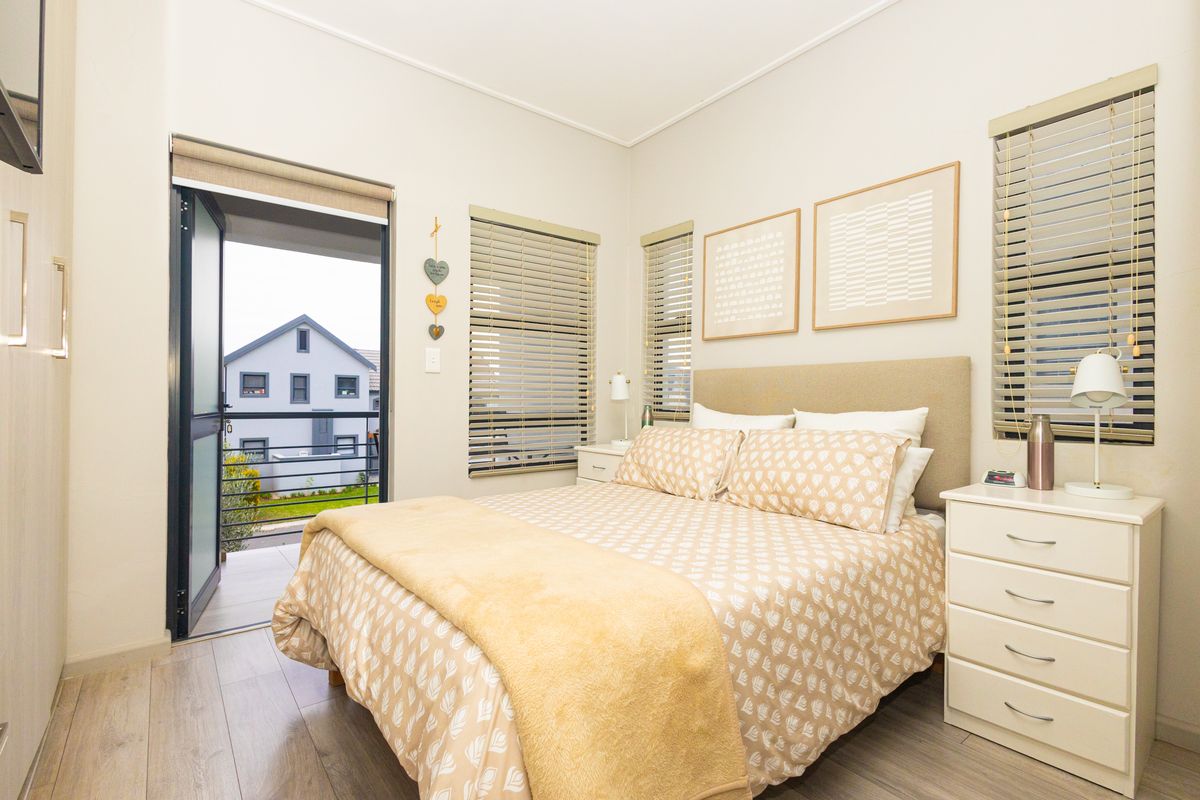 A well-maintained bedroom featuring laminate flooring, venetian blinds, and direct access to a private balcony through a sliding door.