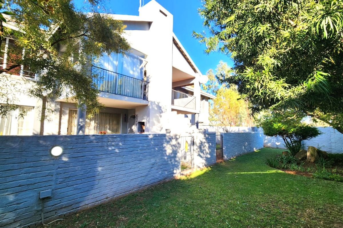 Rear view of the apartment building featuring a private garden, brick boundary wall, and upper-level balconies with metal railings.