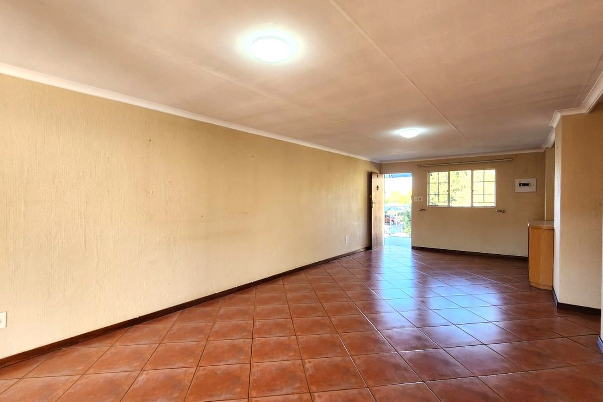 A spacious, empty living area featuring terracotta-style tiled flooring, neutral walls, and built-in cabinetry, offering a blank canvas for personalization.