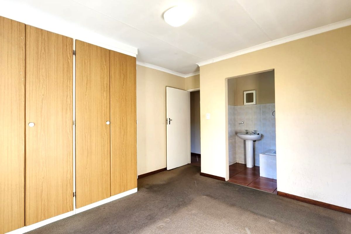 An empty bedroom featuring built-in wooden cupboards, carpeted flooring, and direct access to an en-suite bathroom with a pedestal basin.