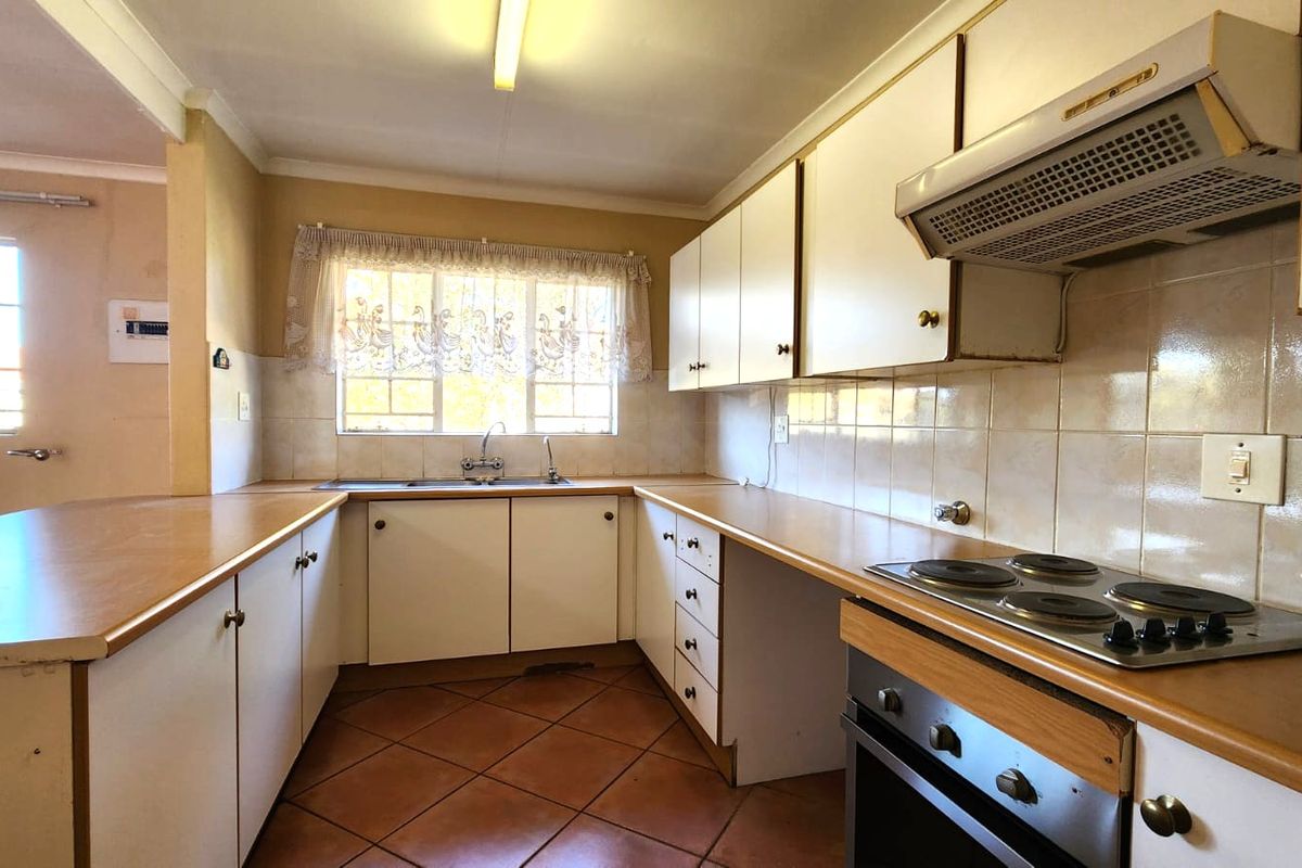 A functional kitchen featuring white cabinetry, laminate countertops, tiled flooring, and built-in cooking appliances, offering a clean space ready for modernization.