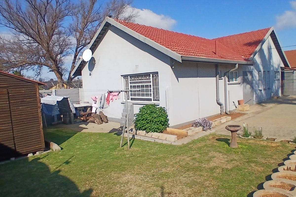 Rear view of the house featuring a tiled roof, concrete driveway, and a private garden area with a storage shed.