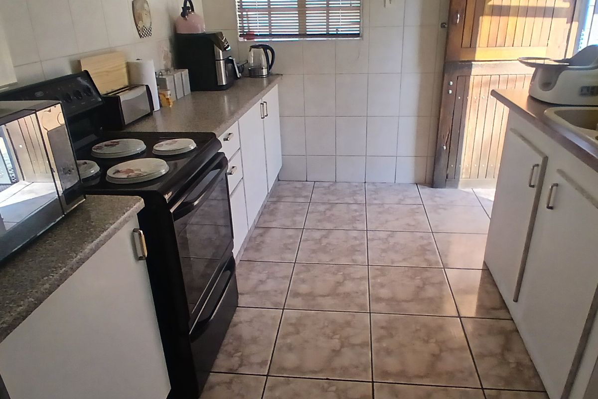 A functional kitchen featuring tiled flooring, wall-mounted cabinetry, a double sink, and a freestanding stove with direct access to an exterior door.