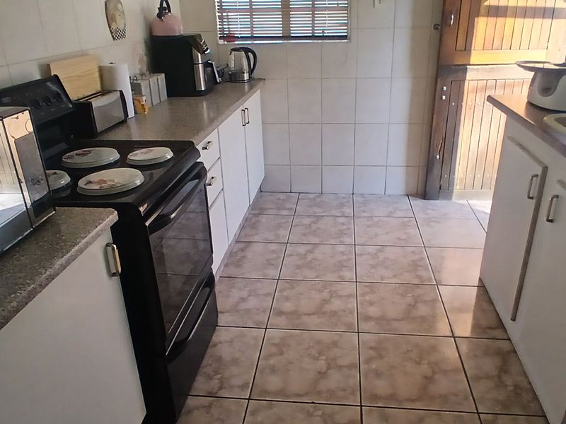 A functional kitchen featuring tiled flooring, wall-mounted cabinetry, a double sink, and a freestanding stove with direct access to an exterior door.