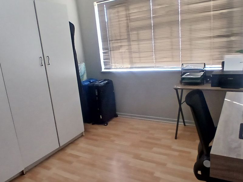 A functional bedroom featuring laminate flooring, built-in wardrobes for storage, and venetian blinds on the window.