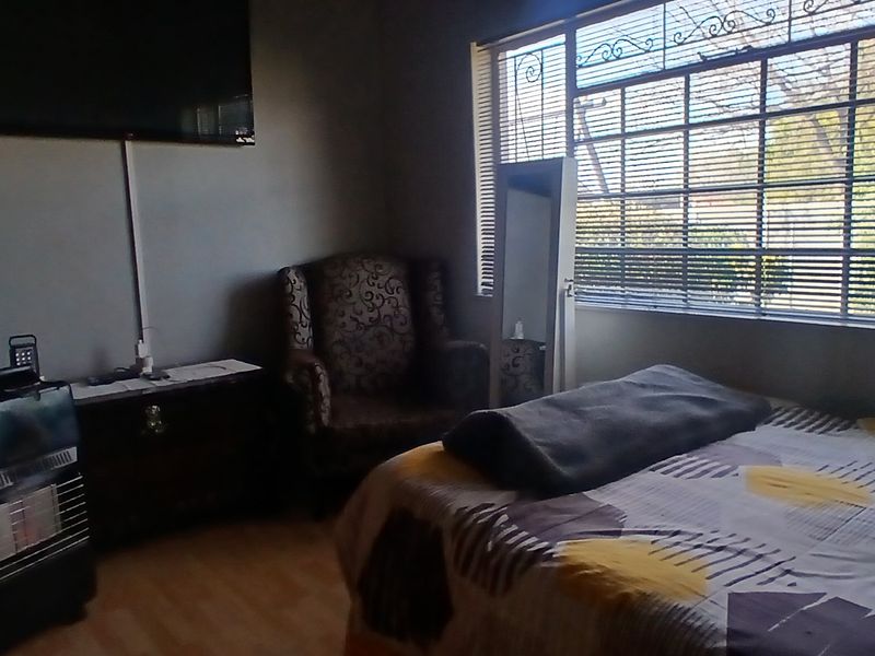 A bedroom featuring laminate flooring and large windows fitted with security bars, providing natural light and ventilation.